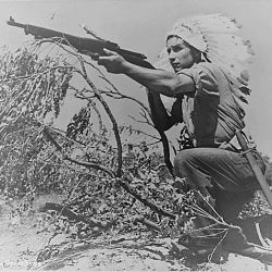 Dan Waupoose, a Menomini chief; full-length, kneeling with a rifle and wearing a feathered headdress, Algiers, Lousiana