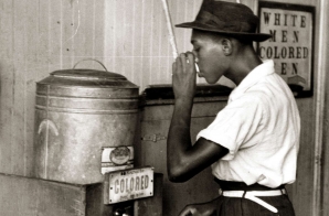 African-American male gets drink from segregated water cooler at the street car terminal
